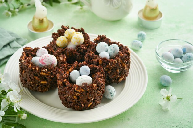 Bolo de ninho de chocolate de Páscoa com mini ovos de chocolate com flores desabrochando de cereja ou maçã na mesa de fundo verde Receita criativa para mesa de Páscoa com decorações de férias Vista superior