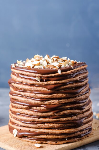 Bolo de panqueca. Uma pilha de panquecas de chocolate com creme de chocolate e amêndoas por cima.