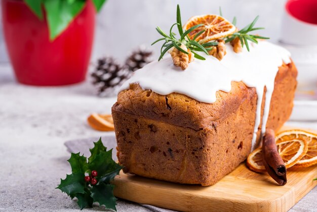 Bolo de pão de frutas polvilhado com glacê, nozes e laranja seca na pedra. Bolo caseiro de férias de Natal e inverno