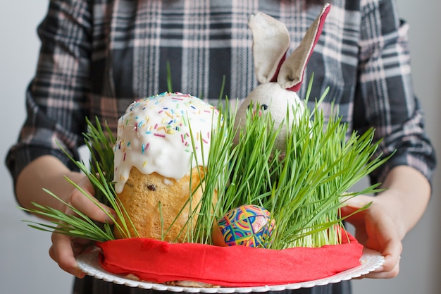 Bolo de Páscoa tradicional, ovos e coelho na grama nas mãos da mulher.