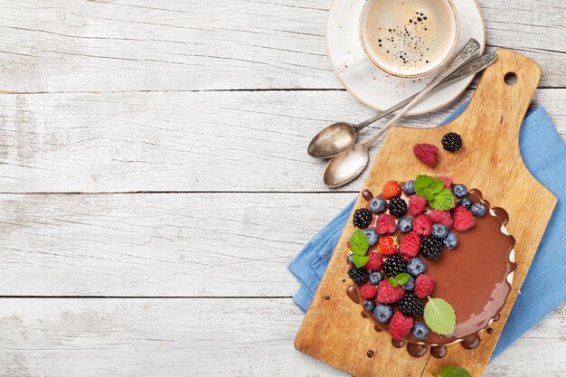 Bolo de queijo de chocolate com bagas e xícara de café Em mesa de madeira com espaço de cópia Vista superior plana