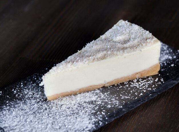 Bolo de queijo de sobremesa coberto com polpa de coco seca, bolo de queijo em uma bandeja individual polvilhado com açúcar de confeiteiro