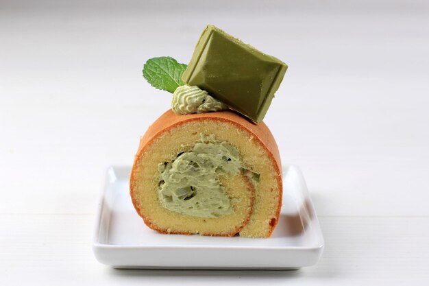 Bolo de rolo de chá verde com chocolate Matcha em cima servido na mesa branca de bolo branco