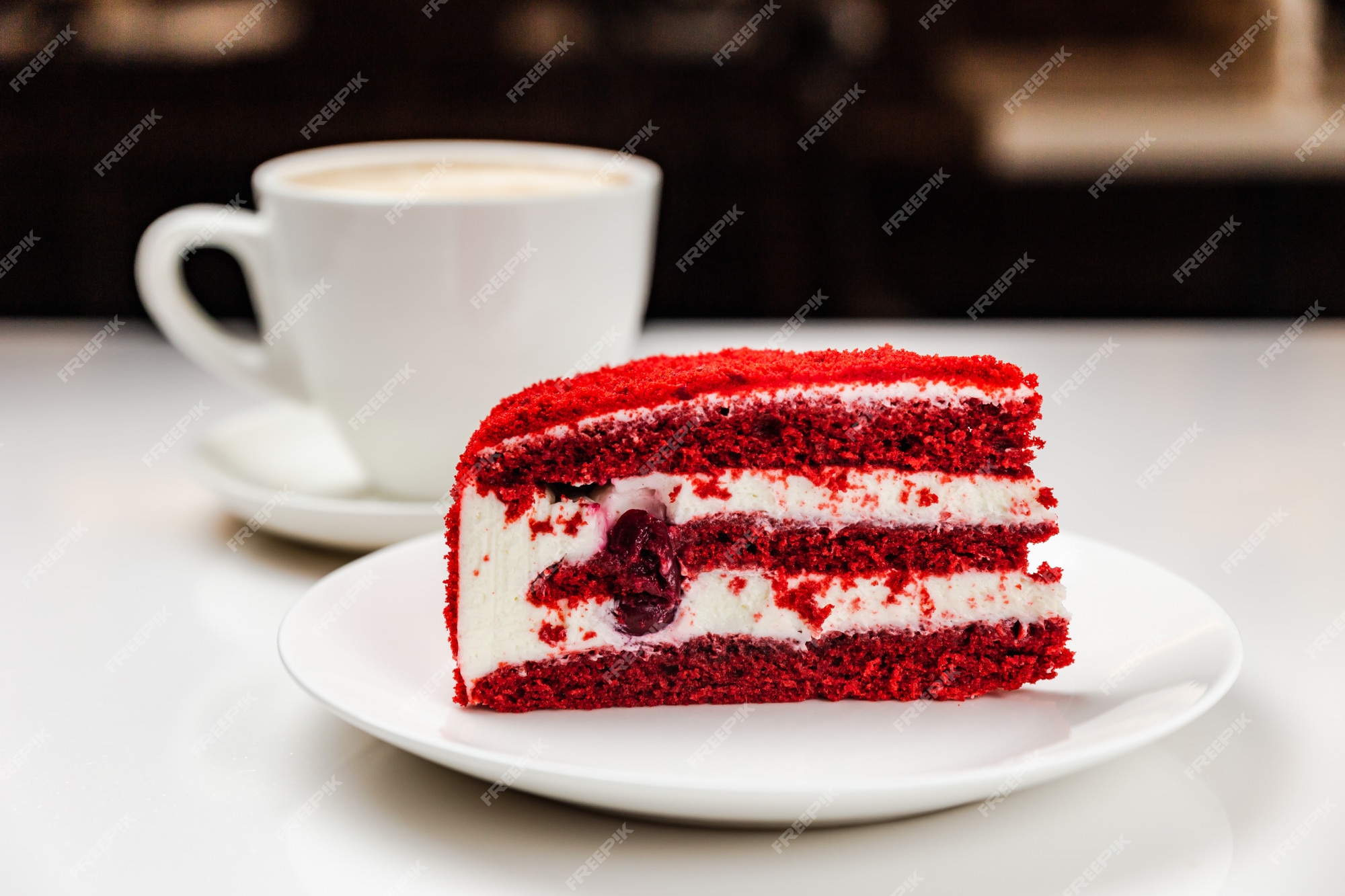 Bolo de veludo vermelho com cereja em um prato branco e uma xícara de café