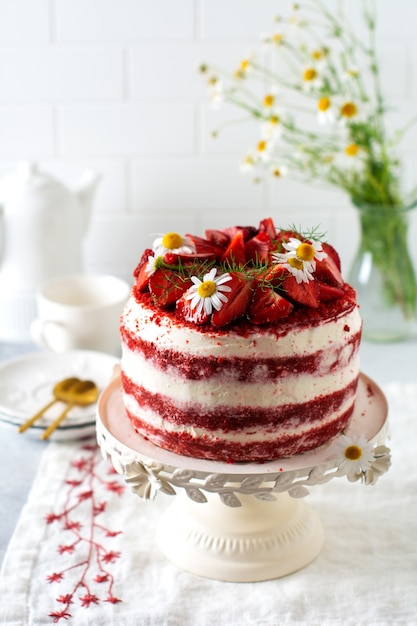 Bolo de veludo vermelho com morango, chantilly e buquê de margaridas no quadro branco sobre fundo cinza. dia dos namorados, sobremesa de casamento ou festa de aniversário. padaria, conceito de confeitaria. copie o espaço.