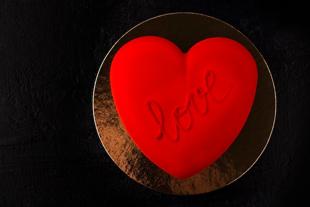 Bolo de veludo vermelho em forma de coração com a inscrição amor em um substrato de ouro e fundo preto. conceito para dia dos namorados, aniversário. copie o espaço