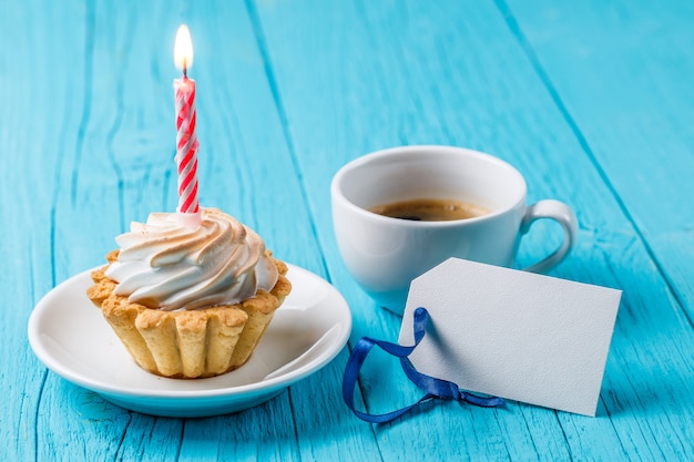 Bolo delicioso com creme e vela acesa caneca de café perfumado cartão vazio na mesa de madeira azul