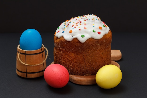 Bolo doce de Páscoa em uma tábua de madeira e ovos de Páscoa coloridos com superfície preta