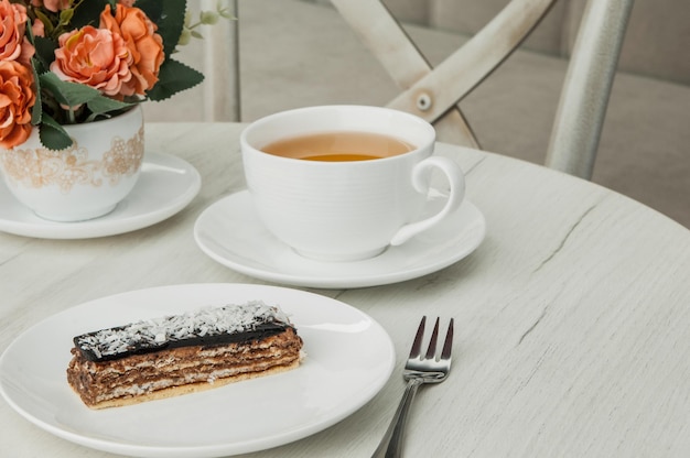 Bolo em um prato e uma xícara de café e um garfo em uma mesa com flores