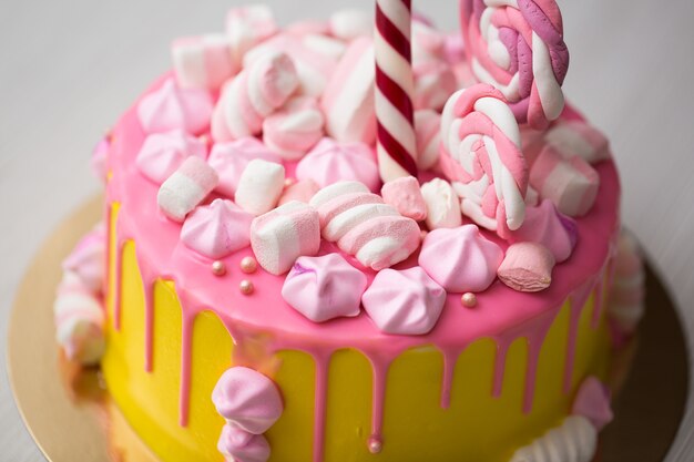 Bolo infantil amarelo com cobertura rosa, merengue e doces