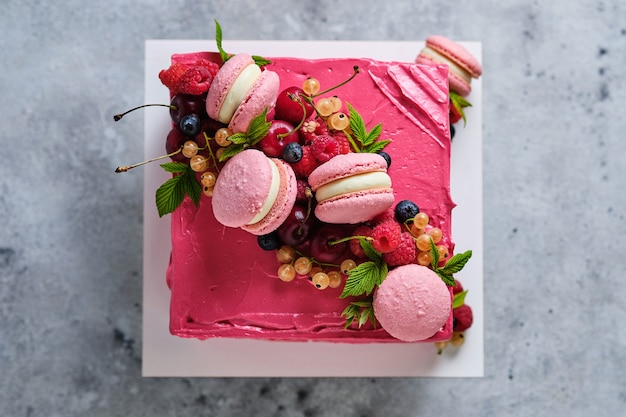 Bolo quadrado rosa decorado com macarons e frutas frescas. bolo para o feriado. a sobremesa é decorada com framboesas frescas, groselhas brancas, cerejas e mirtilos.