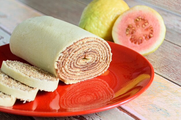 Bolo de rolo cortado en rodajas en un plato rojo junto a guayabas.