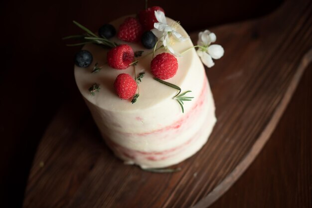 Bolo rosa decorado com bagas e frutas em uma placa de madeira e toalha de mesa boho