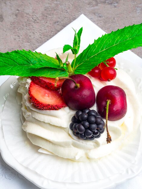 Bolo rústico de Pavlova com morangos frescos, cerejas, amoras, menta e chantilly sobre fundo de concreto