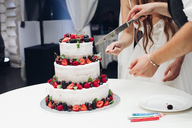 Bolo saboroso de casamento grande incrível com chantilly branco coberto por frutas frescas suculentas e shot completo de frutas. Bela pastelaria em camadas de comida de padaria servindo na mesa em restaurante luxuoso