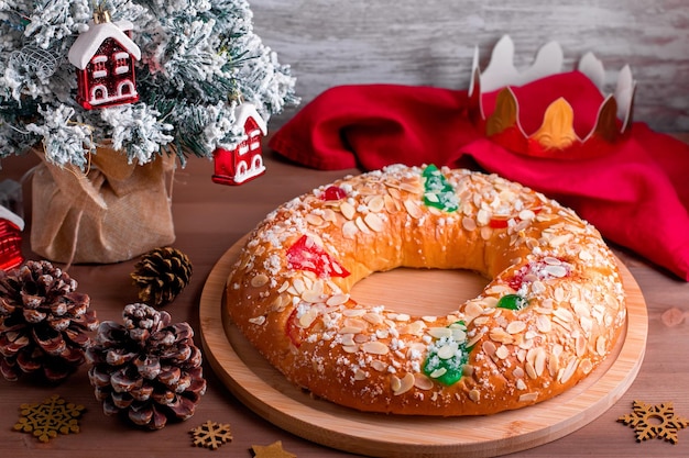 Bolo tradicional da epifania roscon de reyes com coroa de papel no tampo da mesa de madeira com pequena árvore de natal e decoração close up, vista de cima