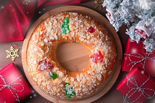 Bolo tradicional da epifania roscon de reyes em mesa de madeira com pequena árvore de natal, presentes embrulhados e decoração closeup, vista de cima