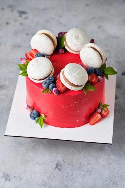 Bolo vermelho para um bolo de menina, decorado com macarons e frutas frescas. Bolo para o feriado. A sobremesa é decorada com morangos frescos, mirtilos e rosas.