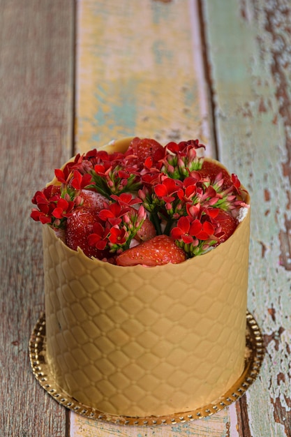 Bolo vestido, envolto em uma camada texturizada de chocolate caramelo salgado, com morangos e flores vermelhas de kalanchoe (foto vertical).