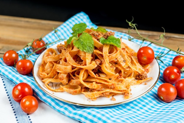 Bolognese em prato em meio a tomates em tecido sobre a mesa