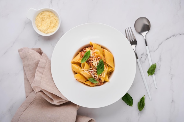 Bolognese-Penne-Nudeln. Leckere appetitliche klassische italienische Penne-Nudeln mit Parmesankäse, Basilikum und Bolognese-Sauce in weißer Platte auf Platte auf Steintisch Traditionelles Gericht der italienischen Küche. Ansicht von oben