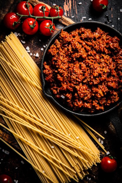 Bolognese-Sauce auf einem Schneidebrett mit Kirschtomaten und trockenen Nudeln