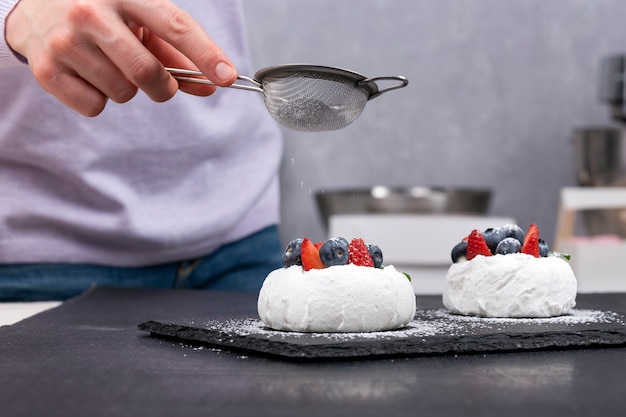 Foto bolos anna pavlova. o chef de confeitaria polvilha açúcar de confeiteiro em bolos de frutas vermelhas.