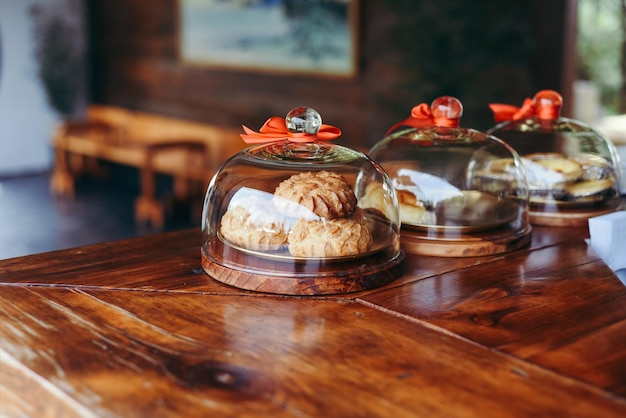 bolos com creme sob tampas de vidro em uma mesa de madeira