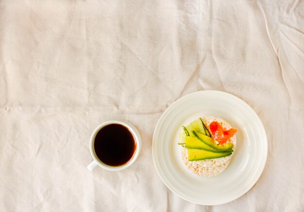 Bolos crocantes de arroz com abacate e salmão fresco com sal. Xícara de café. Vista do topo. Espaço para texto. Refeição rica em proteínas e pobre em carboidratos. Fundo de toalha de mesa de linho branco.