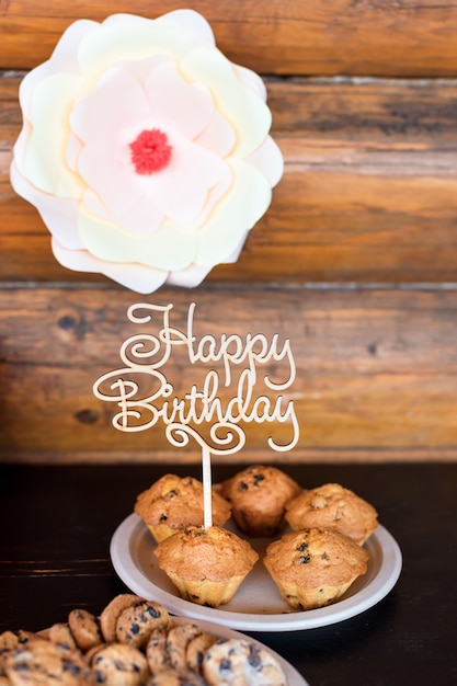 Bolos de aniversário e bolos com sinal de madeira saudação na parede rústica. De madeira cante com letras feliz aniversário e doces de férias.