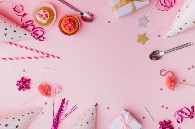 Foto bolos de copo; flâmula; canudos; prop; colher; vela; caixas de presente; chapéu de confete e festa em fundo rosa