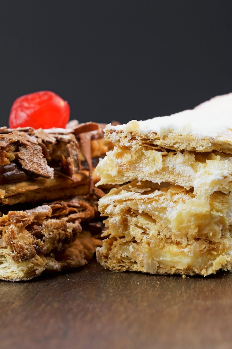 Foto bolos de massa folhada com açúcar de confeiteiro e creme e outro com chocolate e uma cereja em cima da mesa de madeira. feche e espaço para texto. foco seletivo. vertical.
