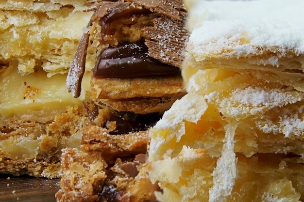 Bolos de massa folhada com açúcar de confeiteiro e creme e outro com chocolate e uma cereja em cima da mesa de madeira. macro close-up. foco seletivo.