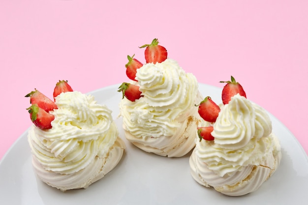 Bolos de merengue com creme de morango e chantilly em um prato em um fundo rosa