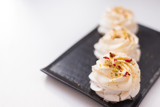 Bolos de merengue em uma placa preta. sobremesa pavlova em um fundo branco. foco seletivo ..