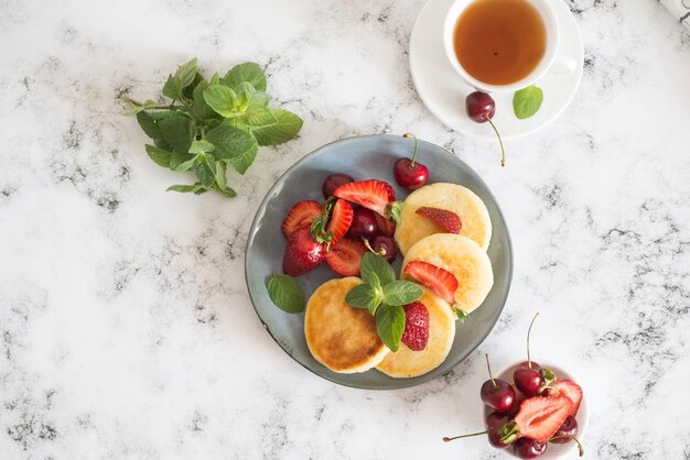 Bolos de queijo cottage com frutas e hortelã em um prato cinza em um fundo de mármore Vista superior