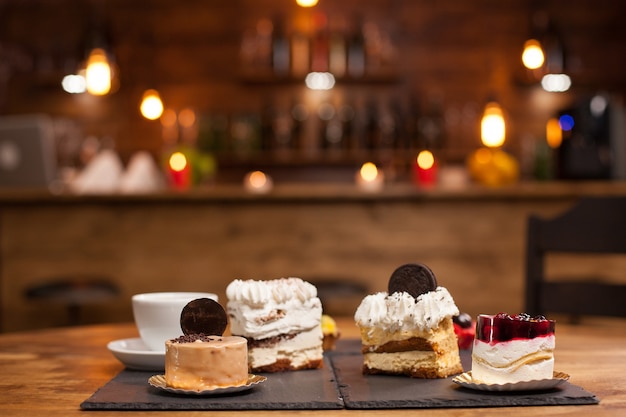 Bolos diferentes com creme de pudim na mesa de madeira em uma cafeteria. Bolo de pudim com frutas vermelhas frescas por cima. Saborosa xícara de café.