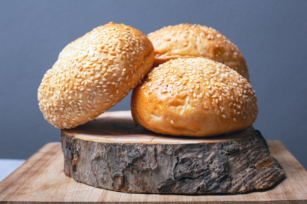 Bolos para fazer hambúrgueres com sementes de gergelim em um carrinho de madeira em um plano de fundo cinza.