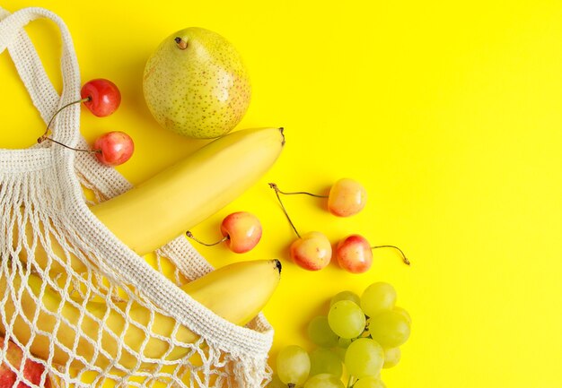 Bolsa de algodón ecológica Frutas maduras en bolsa de malla sobre un fondo amarillo Comida vegana orgánica