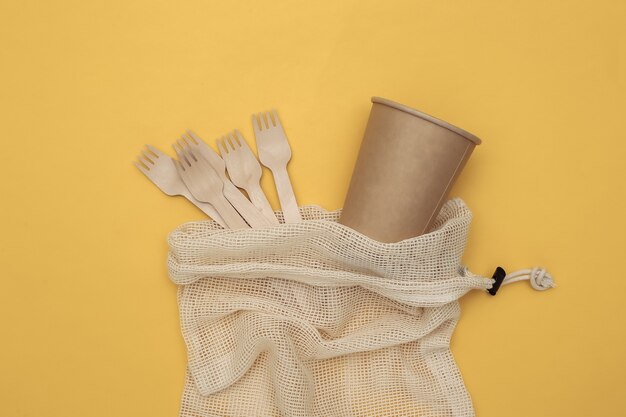 Bolsa de algodón ecológico con cucharas de madera y vaso de cartón sobre fondo amarillo. Concepto ecológico. Vista superior