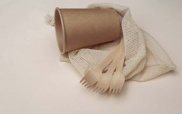 Bolsa de algodón ecológico con cucharas de madera y vaso de cartón sobre fondo beige. Concepto ecológico.