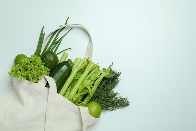 Bolsa de algodón con verduras verdes sobre fondo blanco.