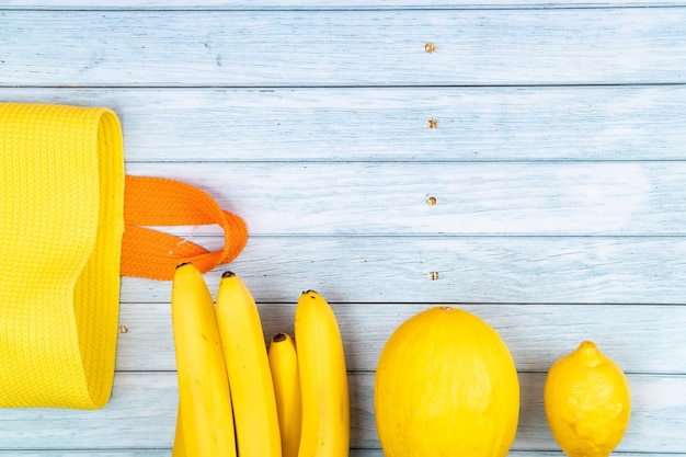 Foto bolsa amarilla y plátanos, melón y limón sobre fondo de madera azul