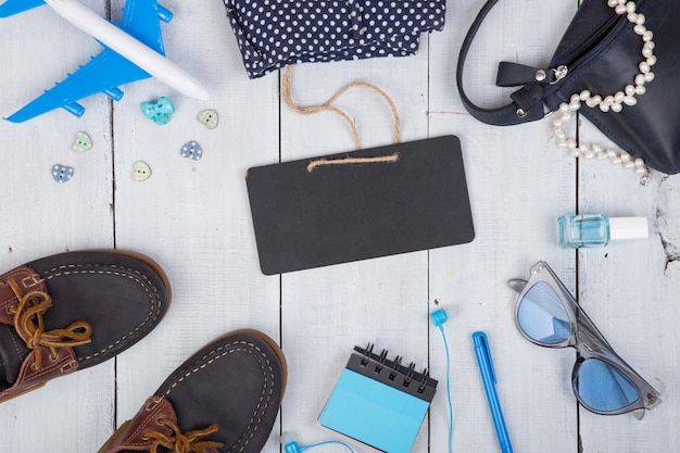 Bolsa azul gafas de sol zapatos esmalte de uñas pizarra en blanco bloc de notas y pequeño avión sobre fondo blanco de madera