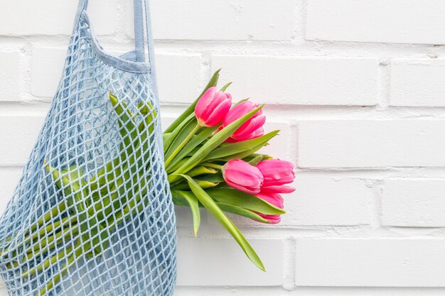 Foto una bolsa azul con tulipanes rosados contra una pared de ladrillo blanco.