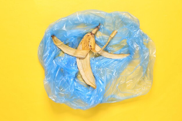 Bolsa de basura y piel de plátano sobre fondo amarillo