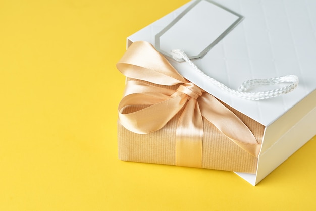 Bolsa blanca con caja de regalo sobre fondo amarillo, vista superior