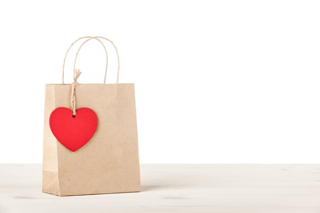 Bolsa de cartón de regalo con etiqueta en forma de corazón sobre fondo blanco.