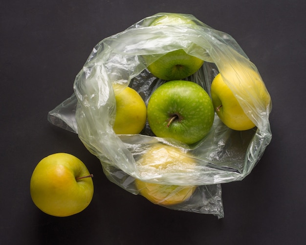 Bolsa de celofán arrugado de plástico transparente con un grupo de manzanas maduras verdes y amarillas sobre un negro