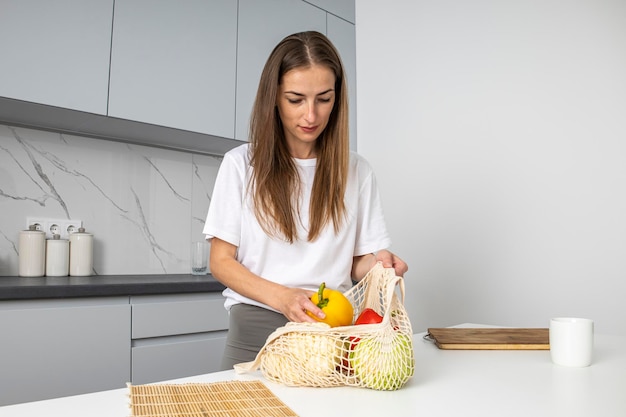 Bolsa de clasificación de mujer joven con verduras frescas en la cocina